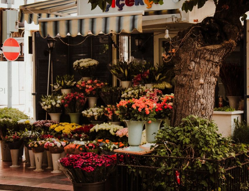 A collection of fresh flower bouquets and potted plants arranged outside a florist shop on Bromley High Street. The flowers include pink, red, white, and yellow chrysanthemums, roses, and lilies, disp